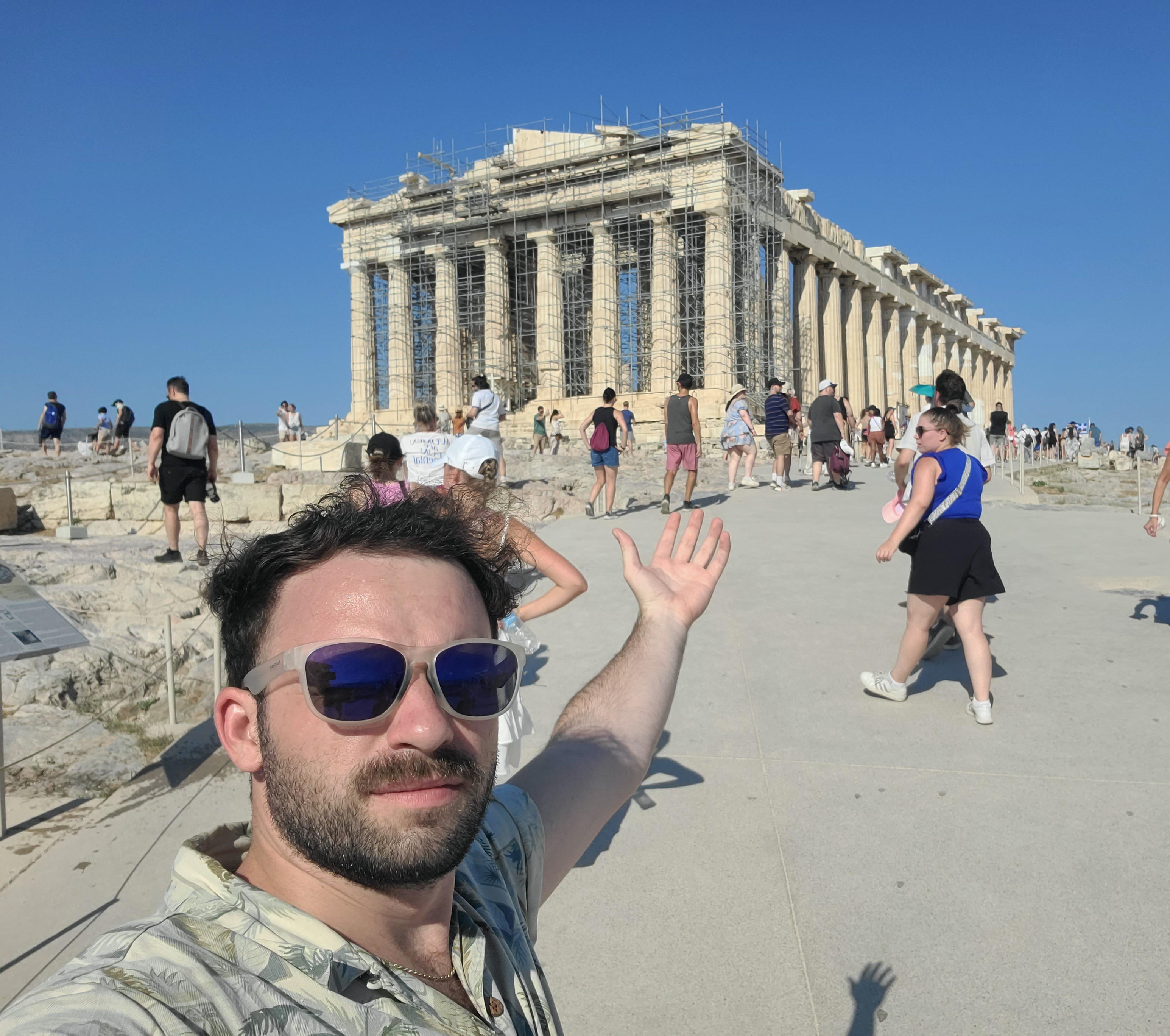 James in front of Greek ruins. Arm extended back reaching towards the ruins.